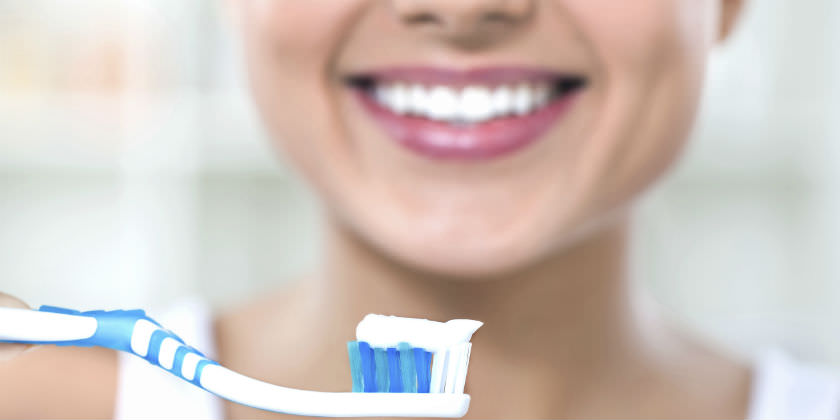 Mujer con el cepillo de dientes en la mano y sonriendo