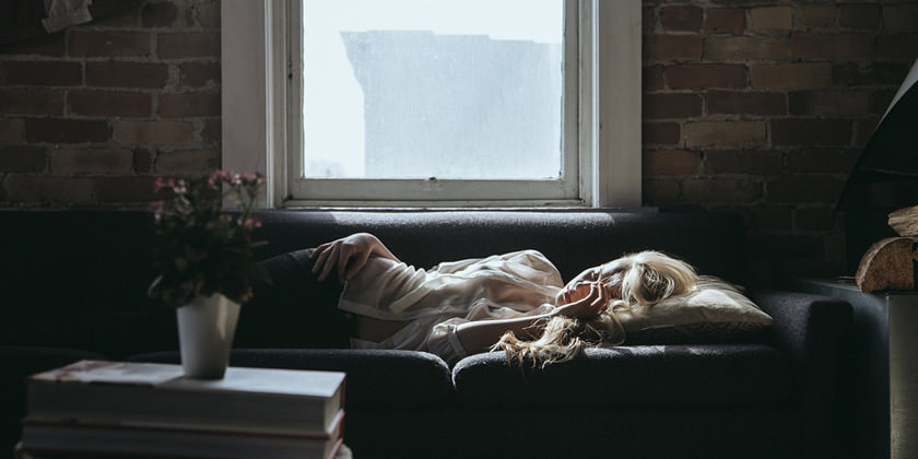 Persona reposando en un sofá con síntomas de cansancio. 
